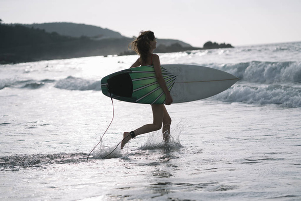 Femme avec planche de surf debout sur la plage de sable mouillé à l'océan
. - Photo, image
