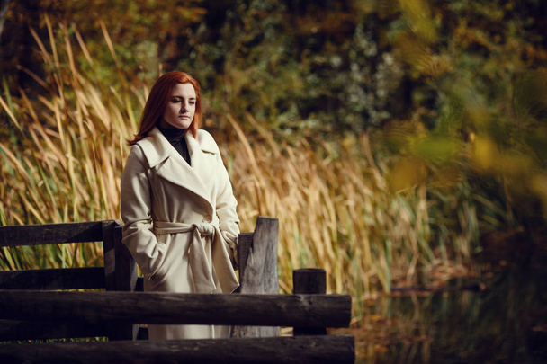 Egy vörös hajú, fehér kabátját ősz gyönyörű, álmodozó és szomorú lány portréja. - Fotó, kép