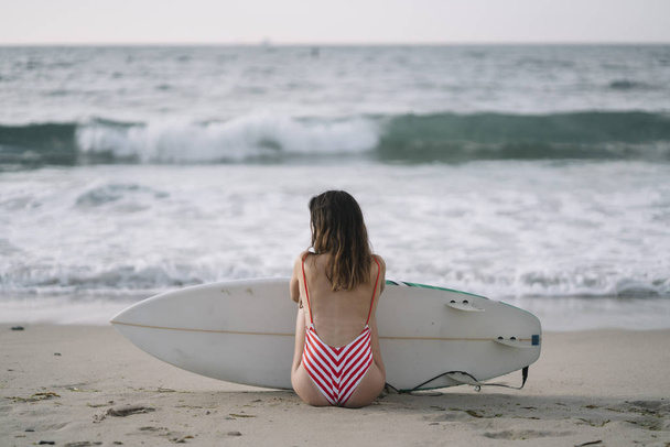 Portrait of a surfer woman on a beach holding a surfboard - Foto, Imagen