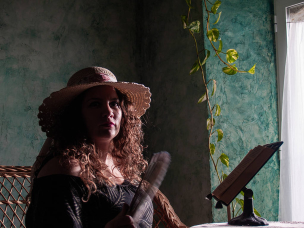 Göndör haja szalma kalap viselése a természetes fény jön be az ablakon egy vidéki ház egy fiatal nő portréja - Fotó, kép