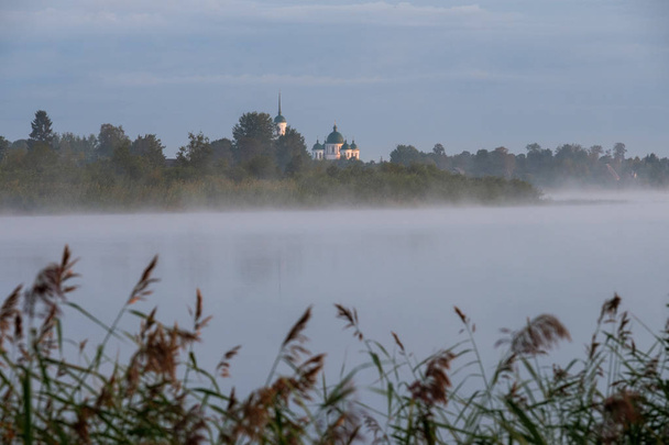 Pohled církve za řekou v mlhavé ráno za svítání. - Fotografie, Obrázek
