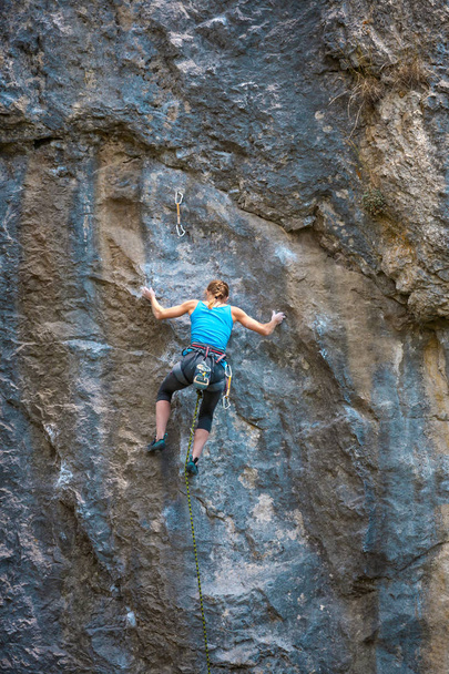 Der Bergsteiger trainiert, um den Felsen zu erklimmen. Ein starkes Mädchen bewältigt eine schwierige Kletterroute. Aktiver Lebensstil. Extremes Hobby. Eine Frau treibt Sport in der Natur. - Foto, Bild