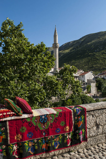 Bosnië-Herzegovina 5/07/2018: de skyline van de stad Mostar, de stad van de Stari Most (oude brug), met kussens, ingericht tapijt op een stenen muur en de minaret van de moskee van Nezir agina dzamija - Foto, afbeelding