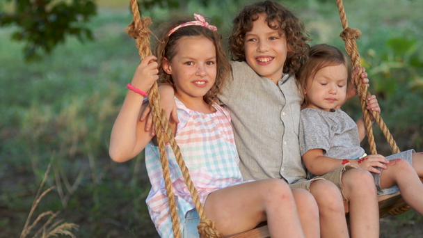 A brother and two younger sisters swing the three of them on a swing. The boy kisses the girl on the cheek, the first love. Summer vacation - Footage, Video