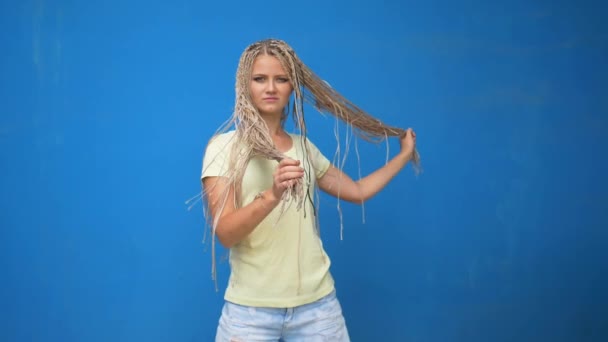 Trendy hipster girl shaking her braided hair pigtails and spinning around on blue background - Filmati, video
