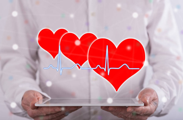 Μια καρδιά που χτυπάει γράφημα έννοια πάνω από ένα tablet που πραγματοποιήθηκε από έναν άνθρωπο στο παρασκήνιο - Φωτογραφία, εικόνα