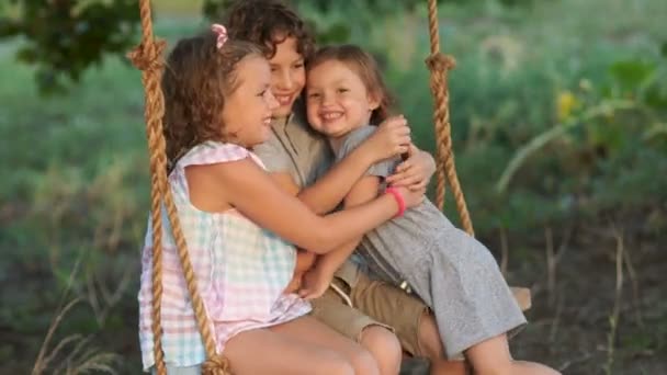 The younger sister resorts to her elder brother and sister to ride on a swing. Happy family, love between brothers and sisters, love of younger children - Footage, Video