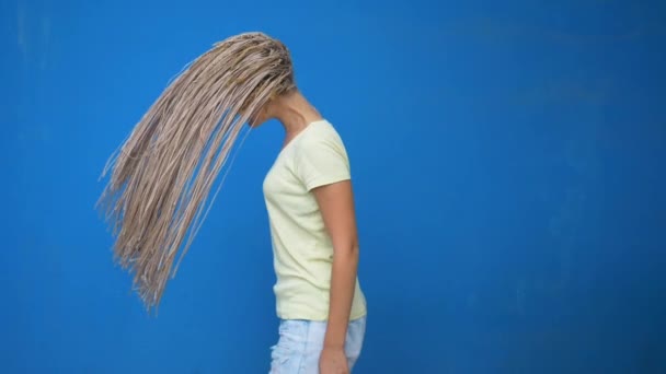 Trendy hipster girl shaking her braided hair pigtails and spinning around on blue background - Metraje, vídeo