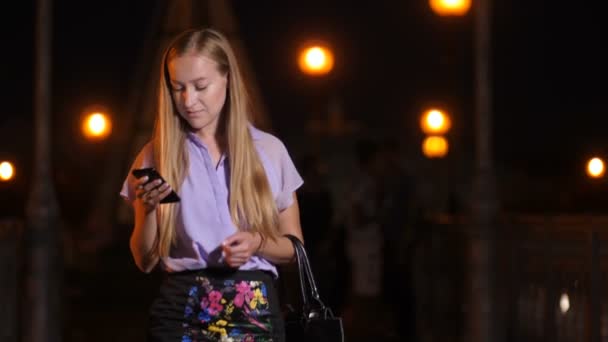 Young woman walking with smartphone and smiling - Footage, Video