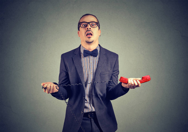 Erwachsener frustrierter Geschäftsmann im Anzug mit rotem Telefonhörer auf grauem Hintergrund - Foto, Bild