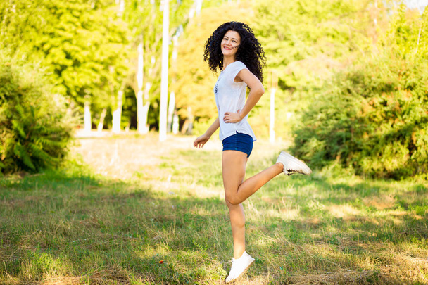 hübsche lockige Frau in Jeans-Shorts springt vor Glück - Foto, Bild