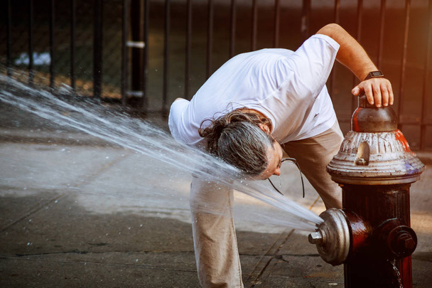 Mann erfrischt sich auf öffentlichem Platz bei sommerlicher Hitze mit Löschwasser - Foto, Bild