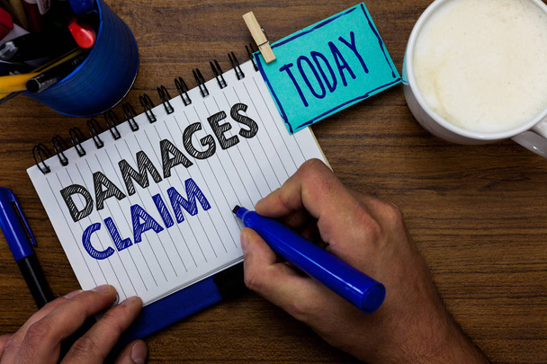 Text sign showing Damages Claim. Conceptual photo Demand Compensation Litigate Insurance File Suit Man holding marker notebook clothespin reminder wooden table cup coffee. - Photo, Image