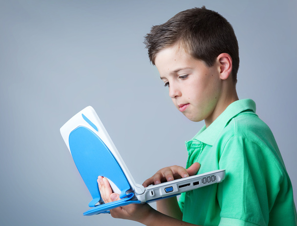 Young casual boy using a laptop against grey background - Фото, изображение