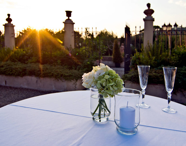 buquê de rosas brancas e hortênsias e dois copos prontos para os amantes iluminados pela luz quente do pôr do sol
 - Foto, Imagem