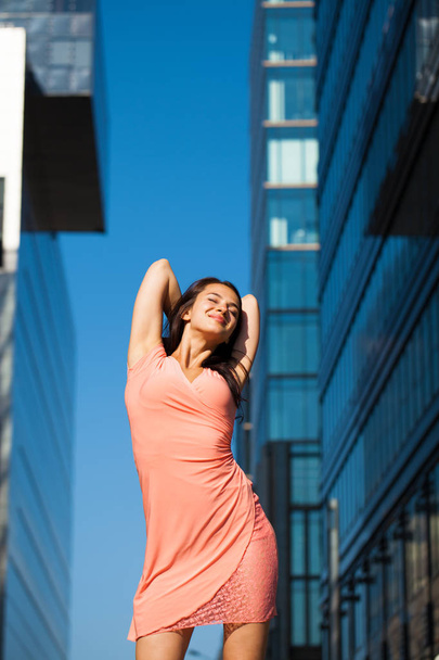 Beautiful young brunette woman in sexy pink dress, against business building street - 写真・画像