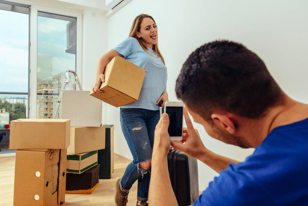 Mann fotografiert seine Freundin beim Halten von Pappschachteln in ihrer neuen Wohnung - Foto, Bild
