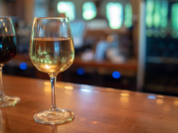 Weißweinglas auf Theke sitzend mit Rotweinglas im Hintergrund - Foto, Bild