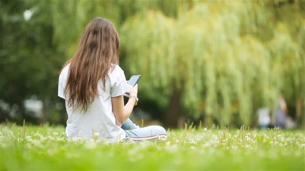 Schattige vrouw leest SMS-bericht op mobiele telefoon tijdens het zitten in het park. - Video