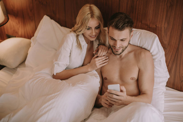 Happy couple in bed at home and use mobile phone - Valokuva, kuva