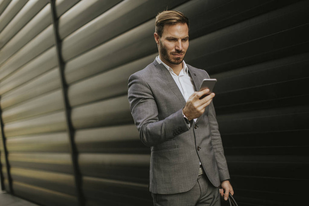 Handsome young businessman walking with mobile phone in front of office building - Fotoğraf, Görsel