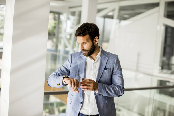 Uomo d'affari in giacca e cravatta, una tazza di caffe 'in un edificio per uffici e guardando l'orologio
 - Foto, immagini