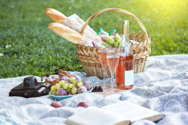Summer - picnic in the meadow.  baguette, wine, glasses, grapes and rolls in a basket on green gras - 写真・画像