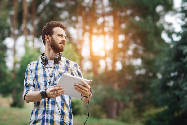 Young bearded hipster with tablet and headphones in the park. - Foto, Imagen