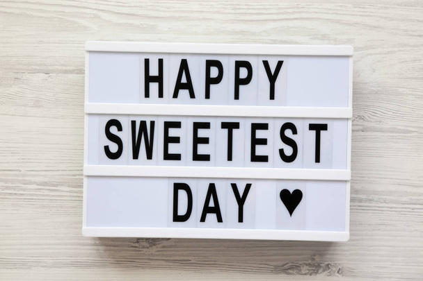 Moderne Tafel mit dem Schriftzug "Happy Sweest Day" über weißer Holzoberfläche, Draufsicht. von oben, flach gelegt, über Kopf.  - Foto, Bild