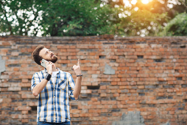 Attractive young bearded hipster with mobile phone pointing up. - Foto, Imagem