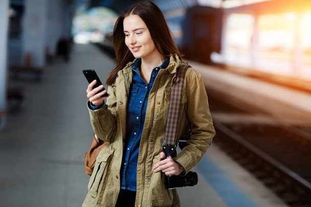 Beautiful young woman using smart-phone while standing on the railway station platform. - Foto, imagen