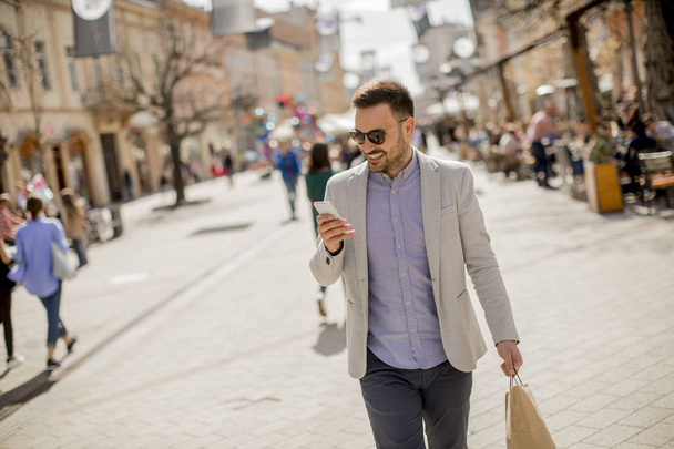 Portrait of cheerful handsome man goes  shopping in the city while uses mobile phone - Fotoğraf, Görsel