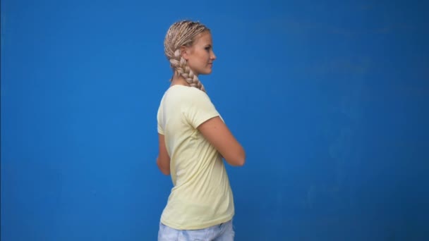 Trendy hipster girl shaking her braided hair pigtails and spinning around on blue background - Felvétel, videó