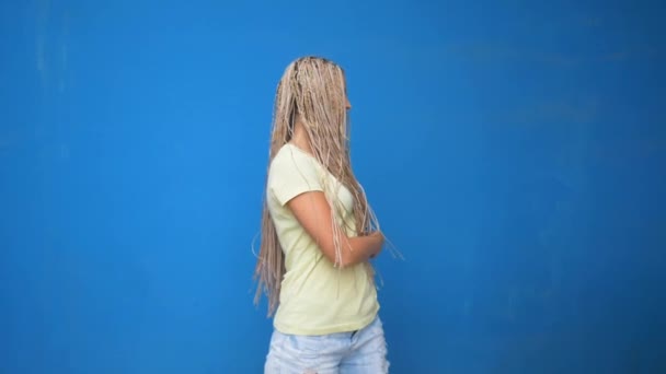 Trendy hipster girl shaking her braided hair pigtails and spinning around on blue background - Video