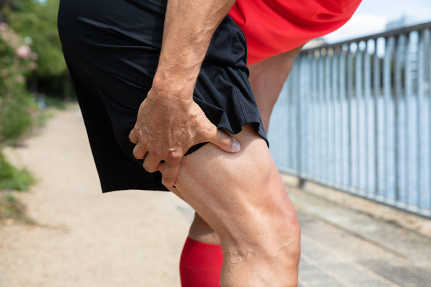 Close-up Of A Male Runner Holding His Injured Leg - Foto, imagen