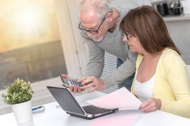 Senior couple checking financial document at home, light effect - Foto, imagen