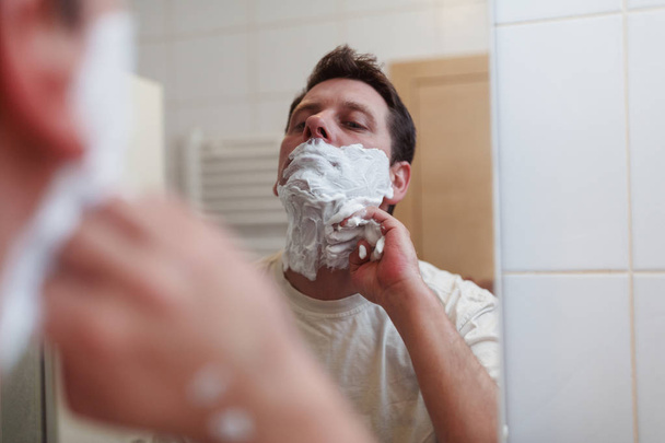 Ochtend hygiëne, gelukkig knap man scheren in badkamer - Foto, afbeelding