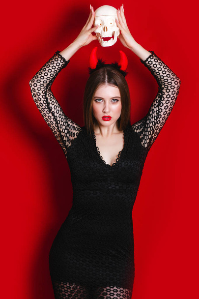 Sensual caucasian young woman with medium brunette hair in devil halloween costume holding skull - Φωτογραφία, εικόνα