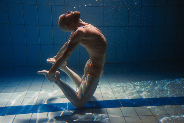 atletische sportman onder water in het zwembad. Sport, yoga, gratis duiken concept - Foto, afbeelding