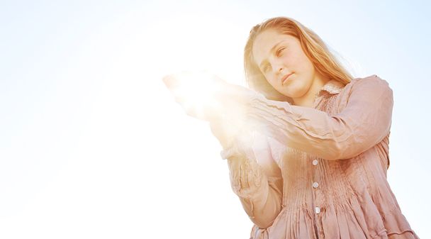 Młoda blond dziewczynka gospodarstwa słońce w jej ręce, z promieniami slonecznymi filtrowanie przeciw błękitne niebo. - Zdjęcie, obraz