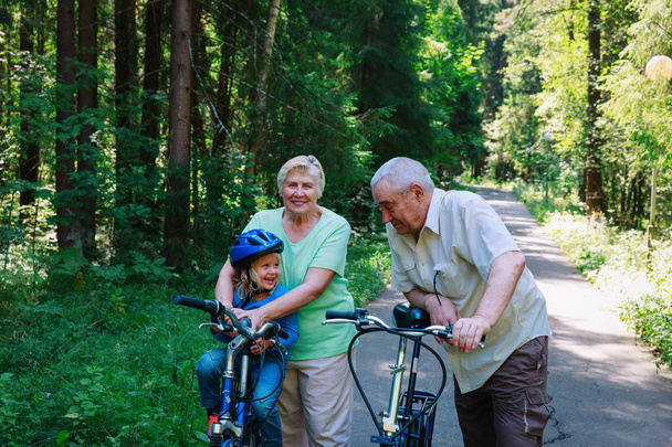 active senior couple with little granddaughter on bikes in nature - Фото, изображение
