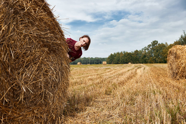 young girl having fun in the field, hiding behind a haystack - Photo, Image