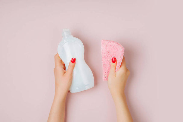Ženské ruce držící čističi a houba na růžovém pozadí - Fotografie, Obrázek