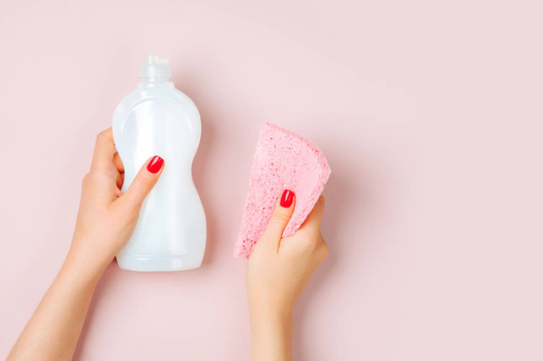 Female hands holding cleanser and sponge on pink background - Zdjęcie, obraz