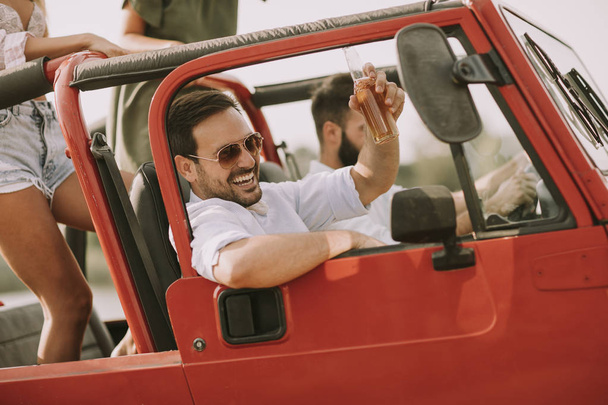 Gruppo di giovani felici godendo viaggio in rosso convertibile e sorridente
 - Foto, immagini