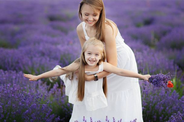Mom and Daughter in the lavender field. Family love concept. Little girl fly in mothers hands. - 写真・画像