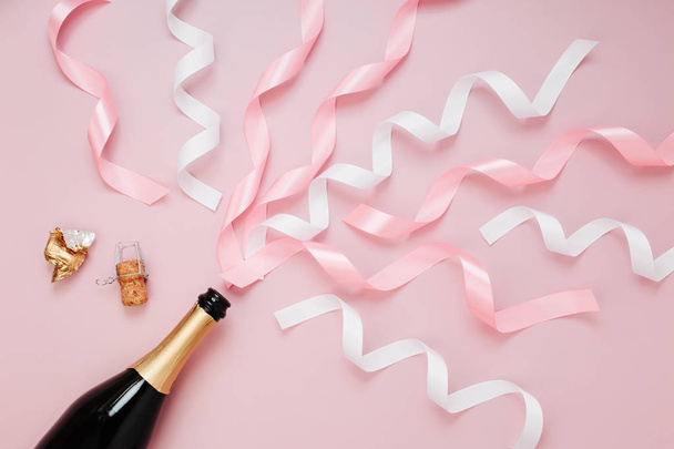 top view of champagne bottle with ribbons on pale pink background - Foto, afbeelding