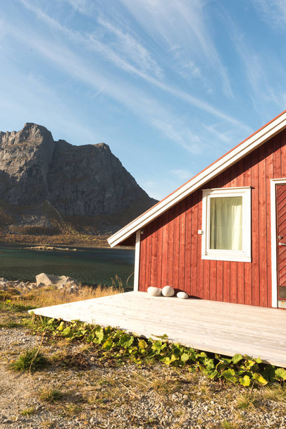 Закройте вид на деревянную пляжную хижину с камнями на короткой линии, выходящей на фьорд, Арктику, Норвегию и горную вершину в солнечный день голубого неба
 - Фото, изображение
