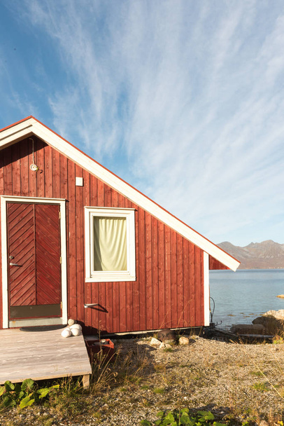 晴れた青い空の日にトロムソ フィヨルド、北極サークル、ノルウェー、山のピークを見渡せる海岸線に石と木のノルウェーのビーチ小屋のトリミング ビューをクローズ アップ - 写真・画像
