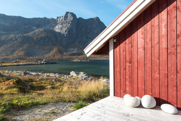 Vue rapprochée d'une cabane de plage norvégienne en bois avec des pierres sur le rivage surplombant le fjord Tromso, le cercle polaire arctique, la Norvège et le sommet de la montagne par une journée ensoleillée de ciel bleu
 - Photo, image